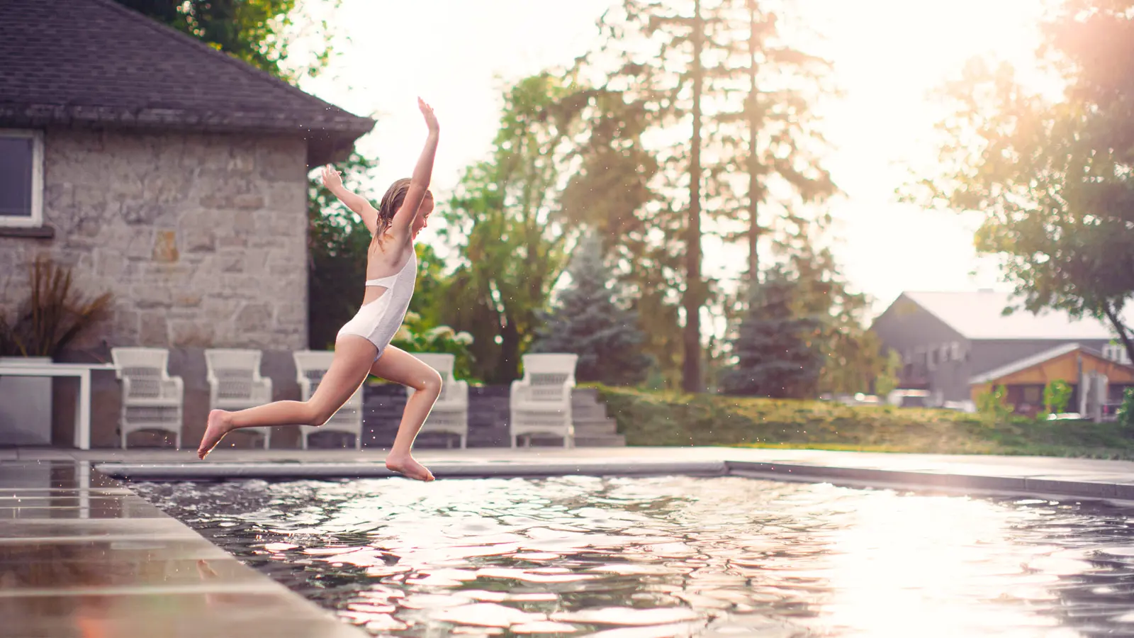 Une jeune fille sautant dans une piscine coque enterrée fabriquée par Leisure Pools